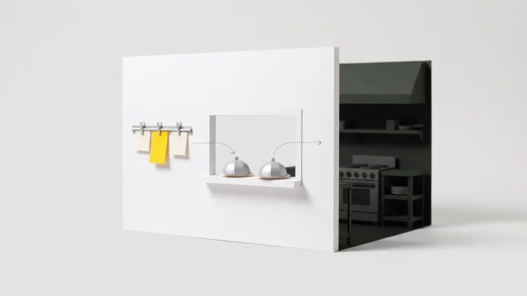 A paper model of a restaurant service window with order tickets on a rail, covered plates on the ledge and a dark kitchen behind the wall